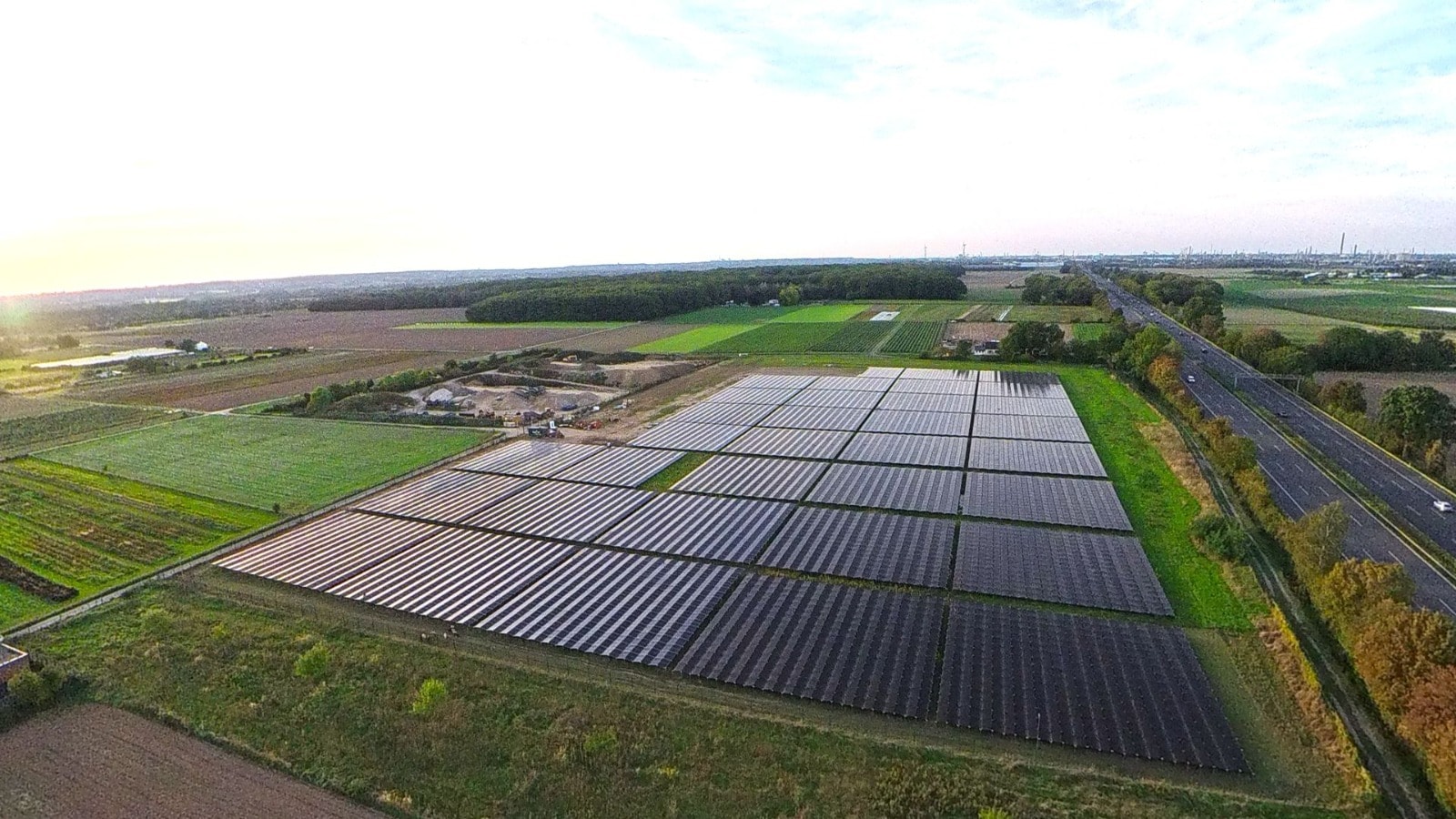 Luftaufnahme einer Photovoltaik-Freiflächenanlage im Abendlicht, eingebettet zwischen Feldern und Autobahn