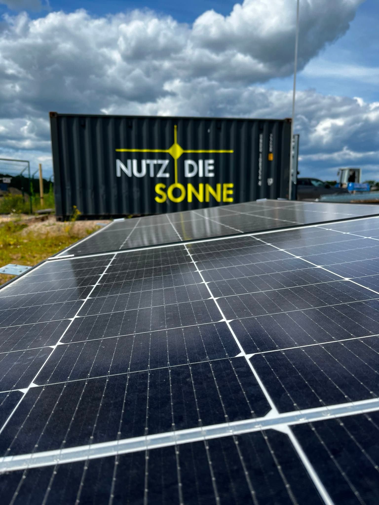 Nahaufnahme eines Solarmoduls, dahinter ein Betriebscontainer